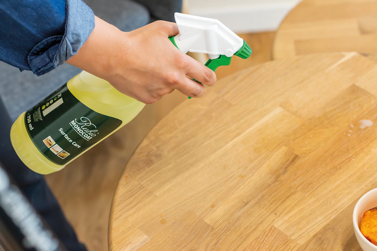 Person using a spray bottle with Rubio Monocoat Surface Care on a wooden surface.